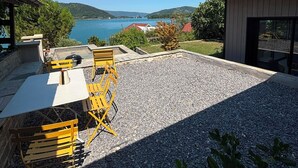 Une terrasse avec des sièges extérieurs, un barbecue et une vue sur un lac et des collines.