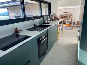 A modern kitchen with a black countertop, a sink, and a window overlooking a garden. - House on the shores of Lake Annecy (Talloires)