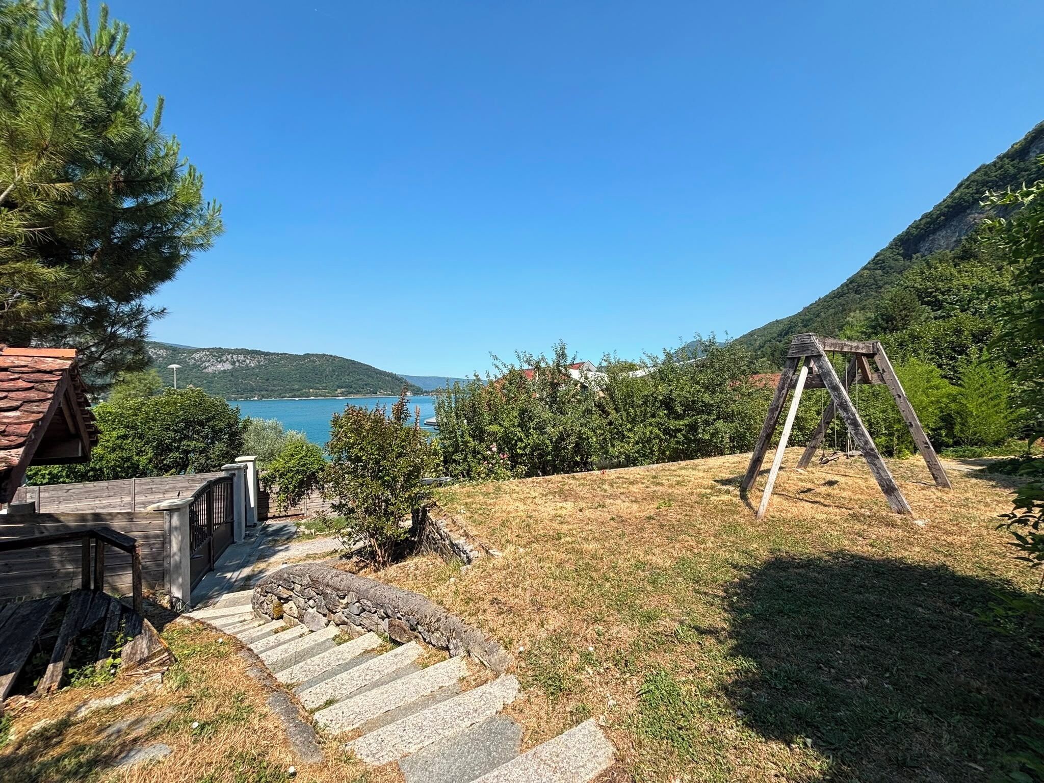 A wooden swing set, stone steps, and a view of a lake and mountains.