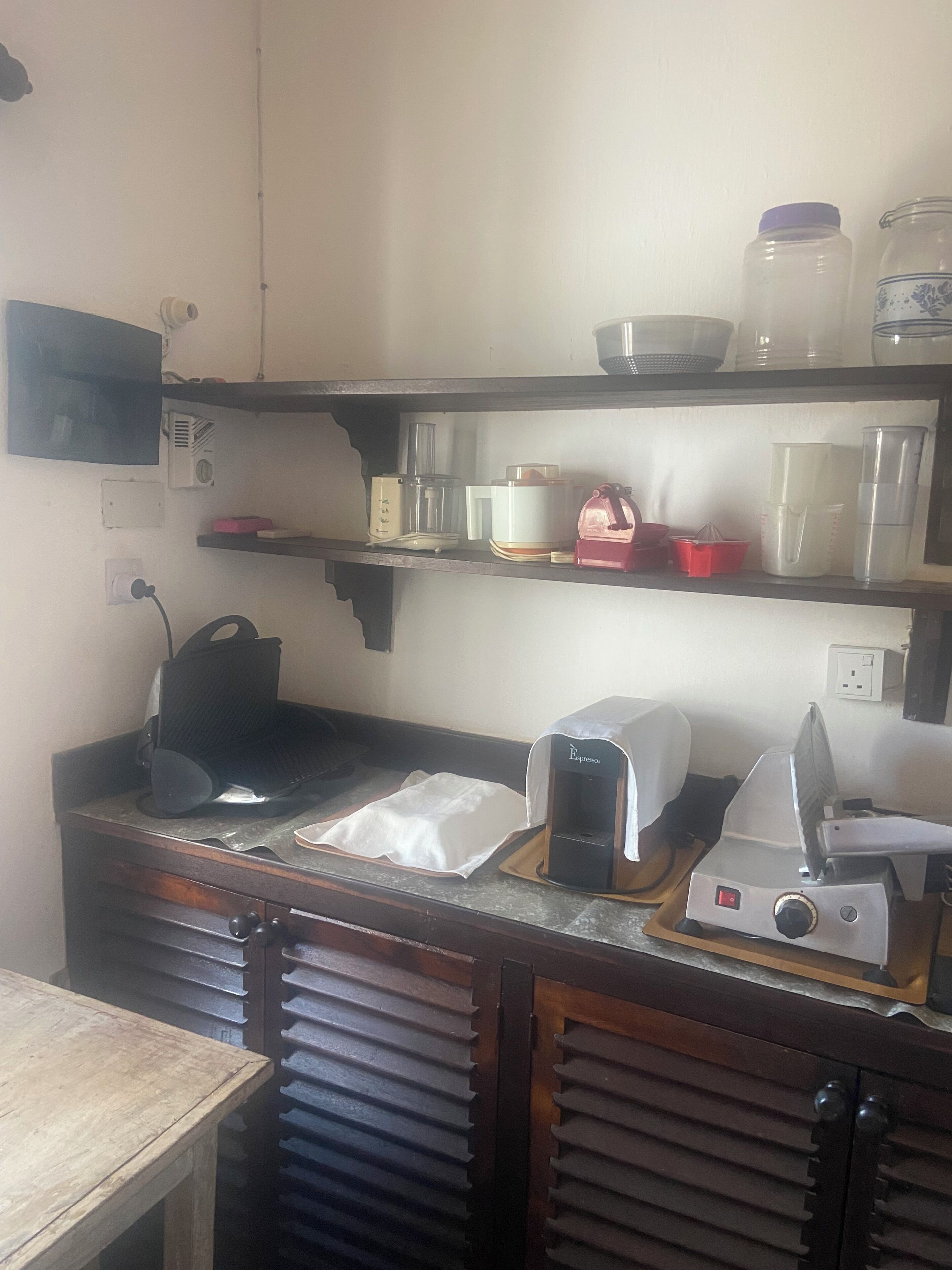 Eine Küche mit einer Kaffeemaschine, einem Toaster und einer Mikrowelle auf der Arbeitsplatte. Darüber befinden sich Regale mit verschiedenen Küchenutensilien.