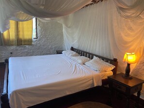 Una cama con ropa de cama blanca, una lámpara de noche y una mesita de madera.