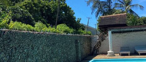 A swimming pool with clear blue water, a stone wall, and a tiled deck area.