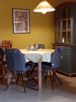 Un coin repas avec une table dressée pour quatre personnes, des chaises, un buffet aux portes vitrées et un tableau encadré au mur.