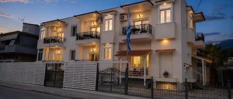 Un edificio residencial de varios pisos con balcones, una bandera y una entrada protegida por un portón.