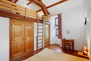 A room with wooden flooring, a loft bed, a desk with a chair, a radiator, and a window with curtains. - Chambres et table d'hôtes de Vernet - Frêne (Saint-Germain-de-Calberte)