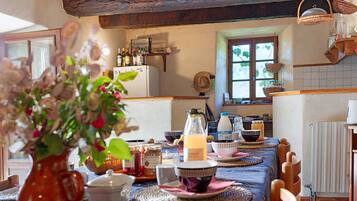 Une cuisine rustique avec des poutres en bois, une table à manger dressée avec des assiettes, des bols et un vase rempli de fleurs.