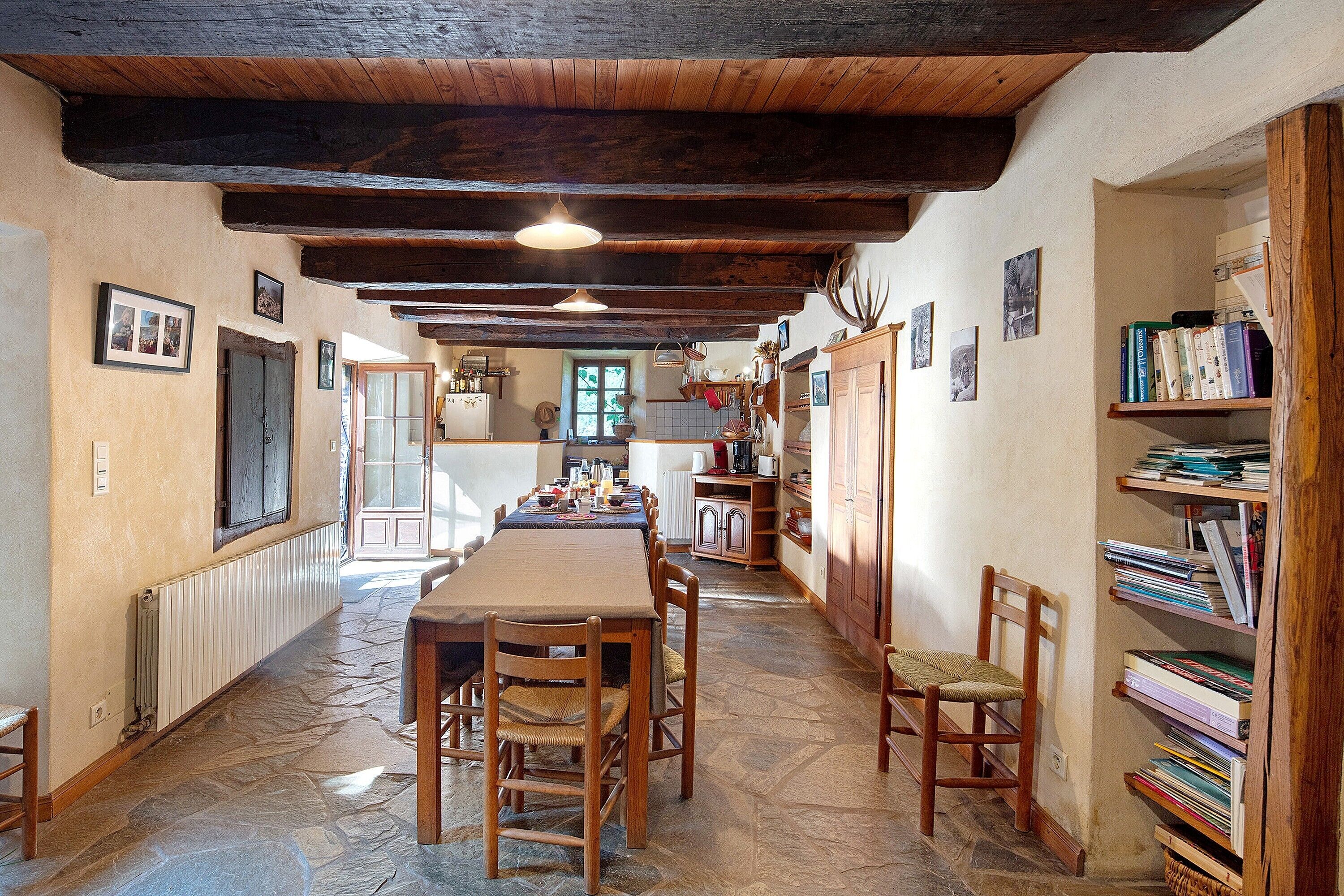 Un comedor rústico con una larga mesa de madera, sillas y piso de piedra.