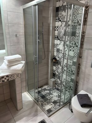 Ein modernes Badezimmer mit einer Duschkabine, einer Toilette und einem Waschbecken mit gestapelten Handtüchern.