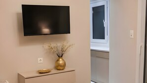 Um quarto com uma cama, televisão na parede, mesa de cabeceira com um vaso e um candelabro.