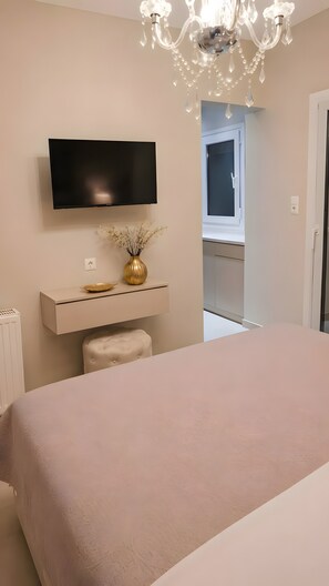 Ein Schlafzimmer mit einem Bett, einem an der Wand befestigten Fernseher, einem Nachttisch mit einer Vase und einer Kristallleuchtre.