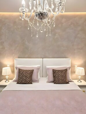 Quarto com lustre, duas mesas de cabeceira, duas luminárias e duas almofadas com estampa de leopardo.