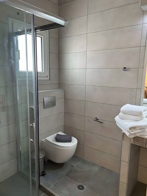 Ein modernes Badezimmer mit Duschkabine aus Glas, Toilette und Waschbeckenbereich mit Handtüchern.