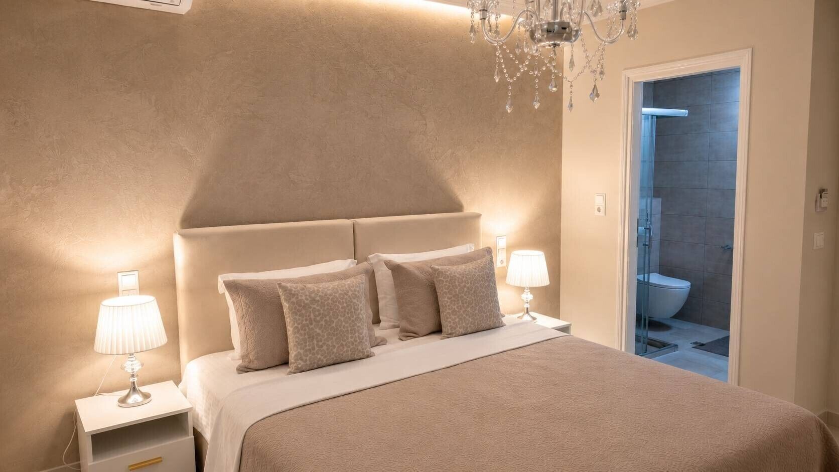 A bedroom with a bed, nightstands, a chandelier, and a bathroom door.