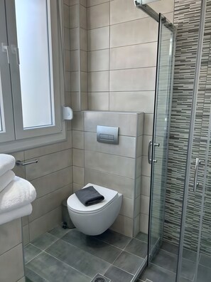 Une salle de bain équipée de toilettes, d’un sèche-mains et d’une douche à parois de verre.