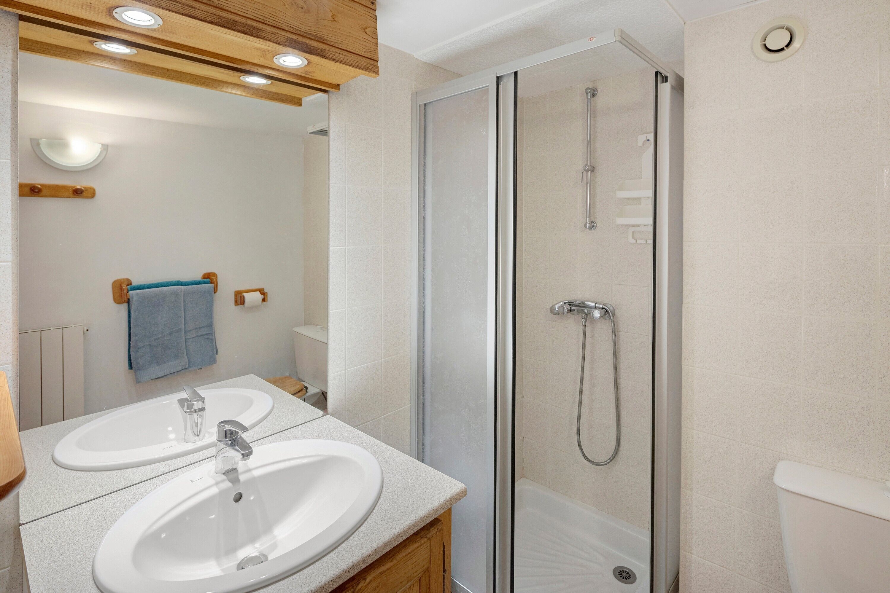 Une salle de bain avec une douche à parois de verre, deux lavabos et un meuble-lavabo en bois.