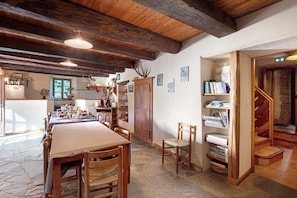 Un comedor rústico con una larga mesa de madera, sillas y una estantería llena de libros.