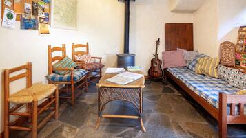 Une pièce chaleureuse avec un sol en pierre, un lit en bois recouvert d’une literie à motifs, une guitare, une table avec des livres et un mur où divers objets sont accrochés.