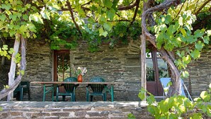 A stone building with a table and chairs outside, surrounded by greenery.