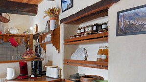 A rustic kitchen with wooden shelves, a kettle, a coffee maker, and various jars.