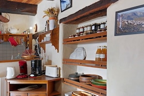Una cocina rústica con estantes de madera, un hervidor, una cafetera y varios frascos.