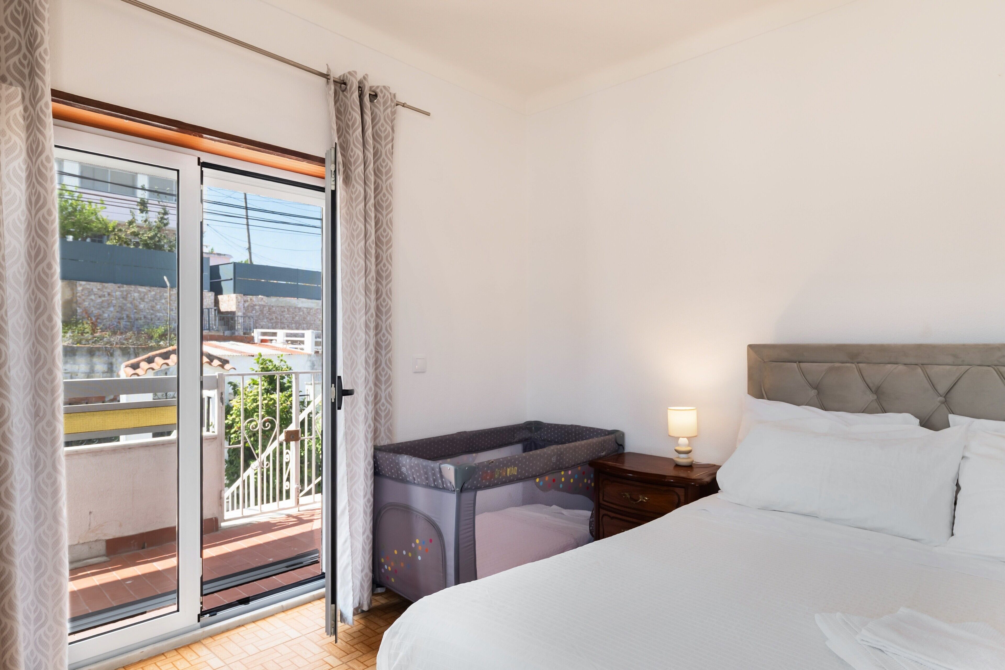 A hotel room with a bed, a nightstand, a lamp, a window with curtains, and a view of the outside.