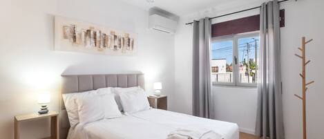 A neatly made bed with white linens, a bedside lamp, and a wall-mounted air conditioning unit.