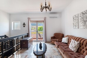 A living room with a sofa, a coffee table, and a chandelier. - Holiday Home 'Vivenda Alves' with Mountain View, Wi-Fi and Air Conditioning (Charneca da Caparica)