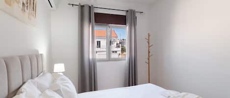 Een hotelkamer met een bed, een bedlampje, een raam met gordijnen en een kapstok.
