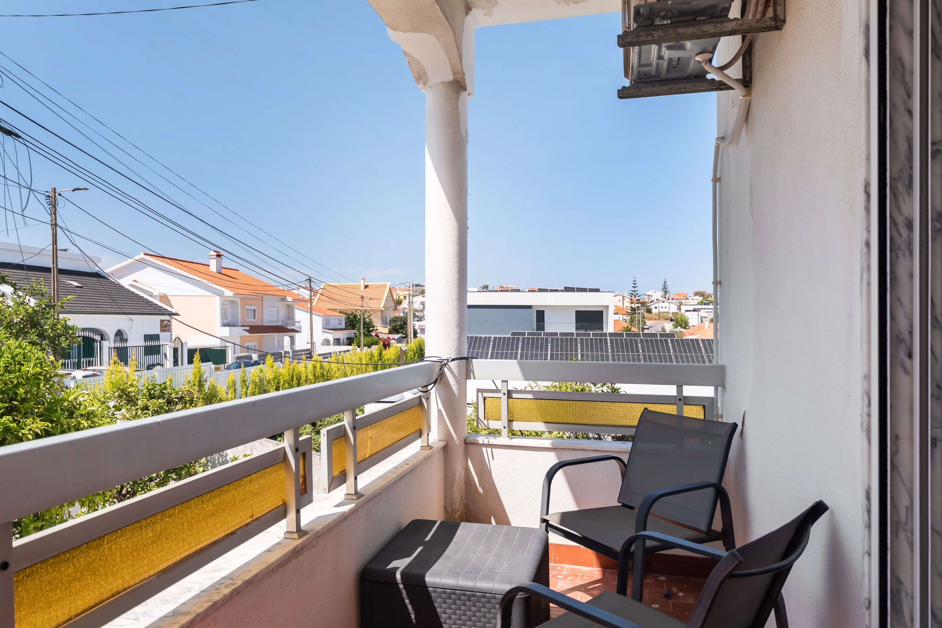 En balkon med et bord og stole, udsigt over et boligområde med huse og en klar himmel.