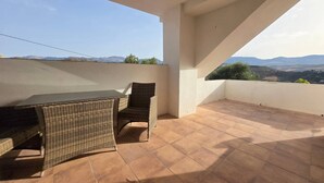 Una terraza con mesa y sillas, vista al paisaje y cielo despejado.
