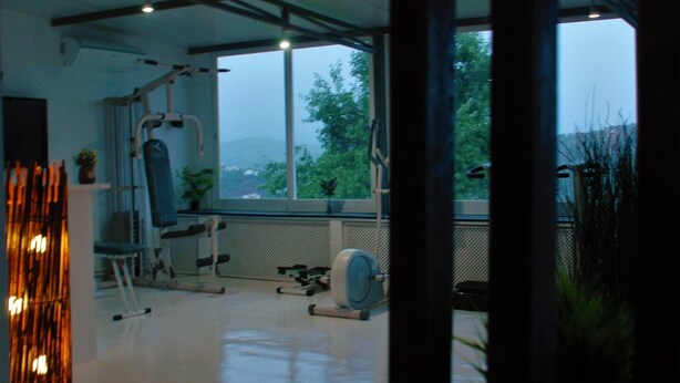 Un gimnasio con equipo de ejercicio, un amplio ventanal y vistas a árboles.