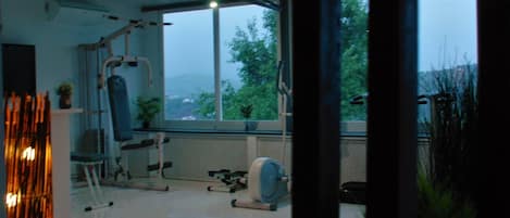 A gym with exercise equipment, a large window, and a view of trees.