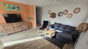 Una sala de estar con un sofá, una mesa de centro, un televisor sobre un mueble de madera y un ventilador.