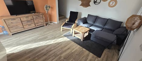 Een woonkamer met een bank, een salontafel, een televisie op een houten kast, en een ventilator.
