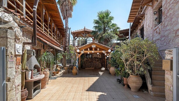 Un estrecho callejón con edificios de piedra tradicionales, una pérgola de madera y plantas en macetas.