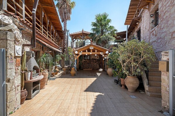 Un estrecho callejón con edificios de piedra tradicionales, una pérgola de madera y plantas en macetas.