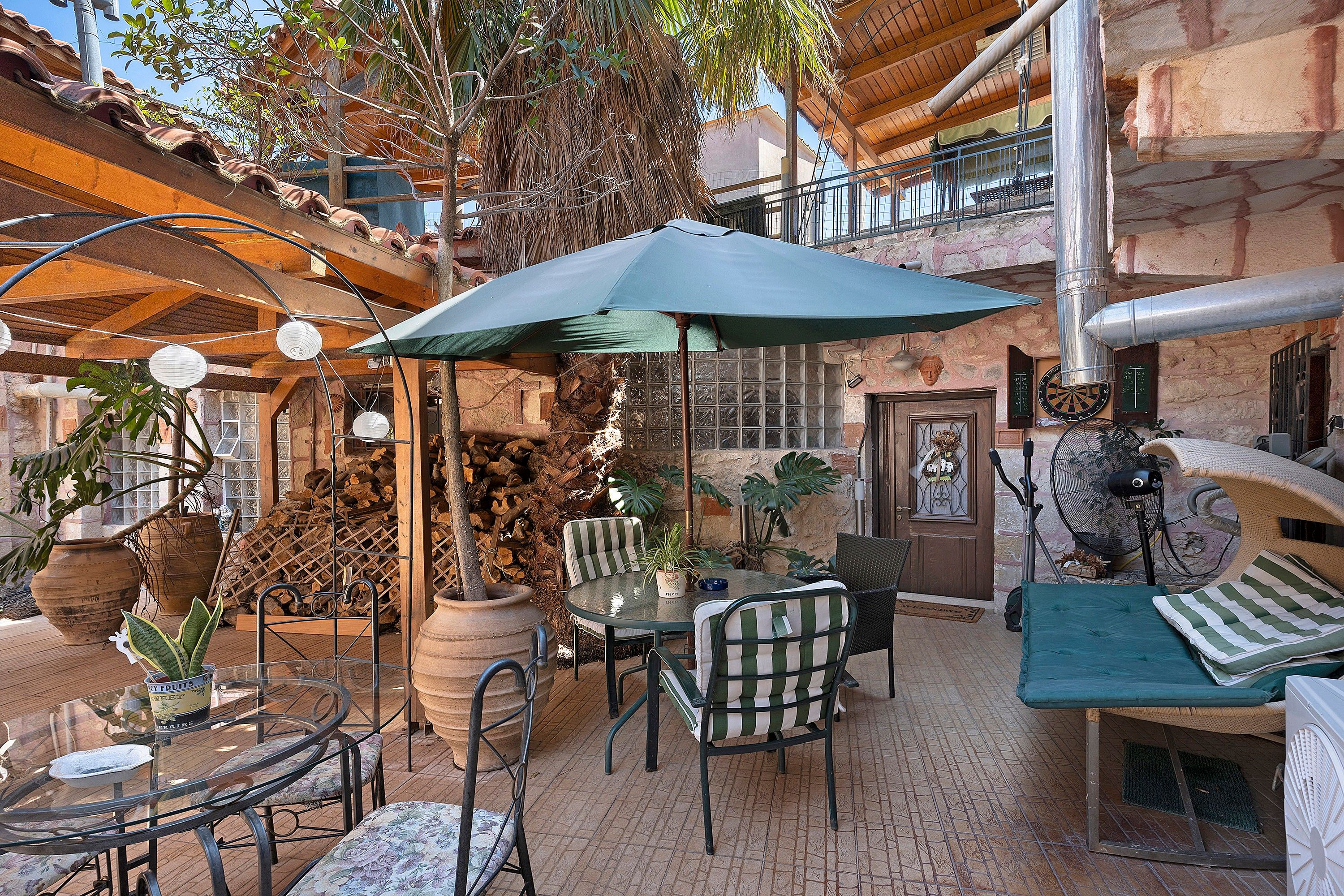 Ein Terrassenbereich im Freien mit Tisch und Stühlen, einem großen Sonnenschirm und verschiedenen Kübelpflanzen.