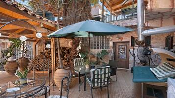 Ein Terrassenbereich im Freien mit Tisch und Stühlen, einem großen Sonnenschirm und verschiedenen Kübelpflanzen.