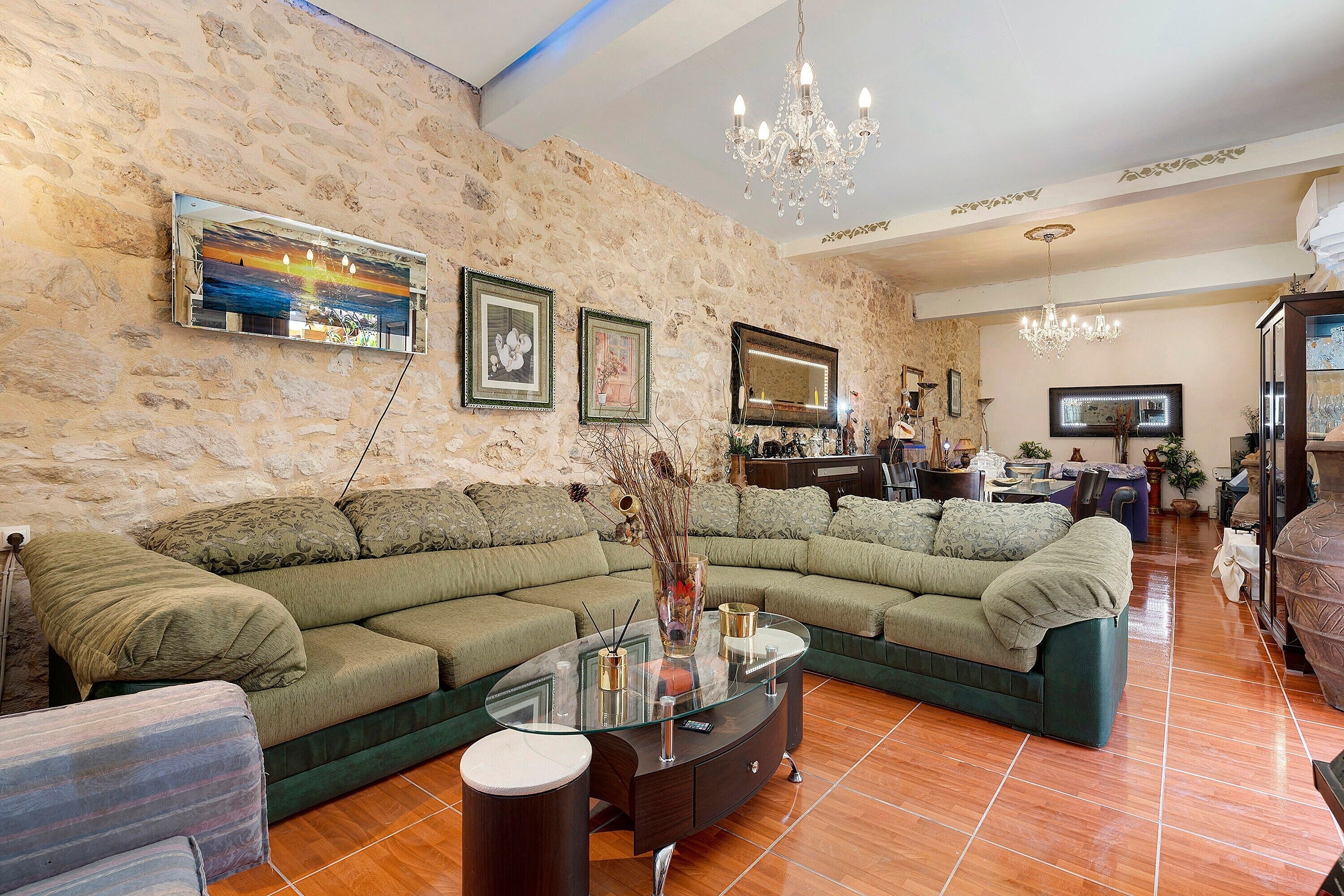 A spacious living room with a large sectional sofa, a glass coffee table, and a stone wall.