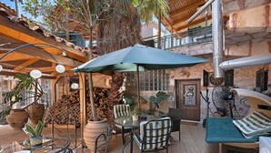 Un espacio al aire libre con patio, mesa, sillas, un paraguas grande y varios maceteros con plantas.