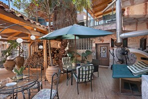 Un espacio al aire libre con patio, mesa, sillas, un paraguas grande y varios maceteros con plantas.
