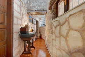 Un pasillo estrecho con paredes de piedra, una puerta de madera, un lavabo y una ventana con vistas.