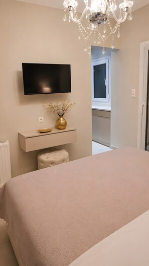 Ein Schlafzimmer mit einem Bett, einem an der Wand montierten Fernseher, einem kleinen Tisch mit einer Vase und einer Pendelleuchte.