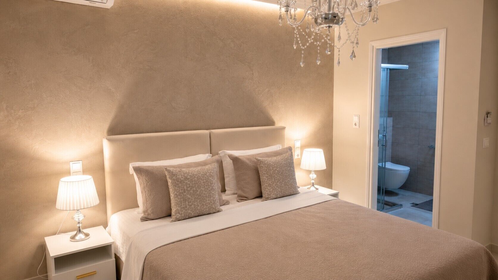 A bedroom with a bed, nightstands, lamps, a chandelier, and a bathroom door.