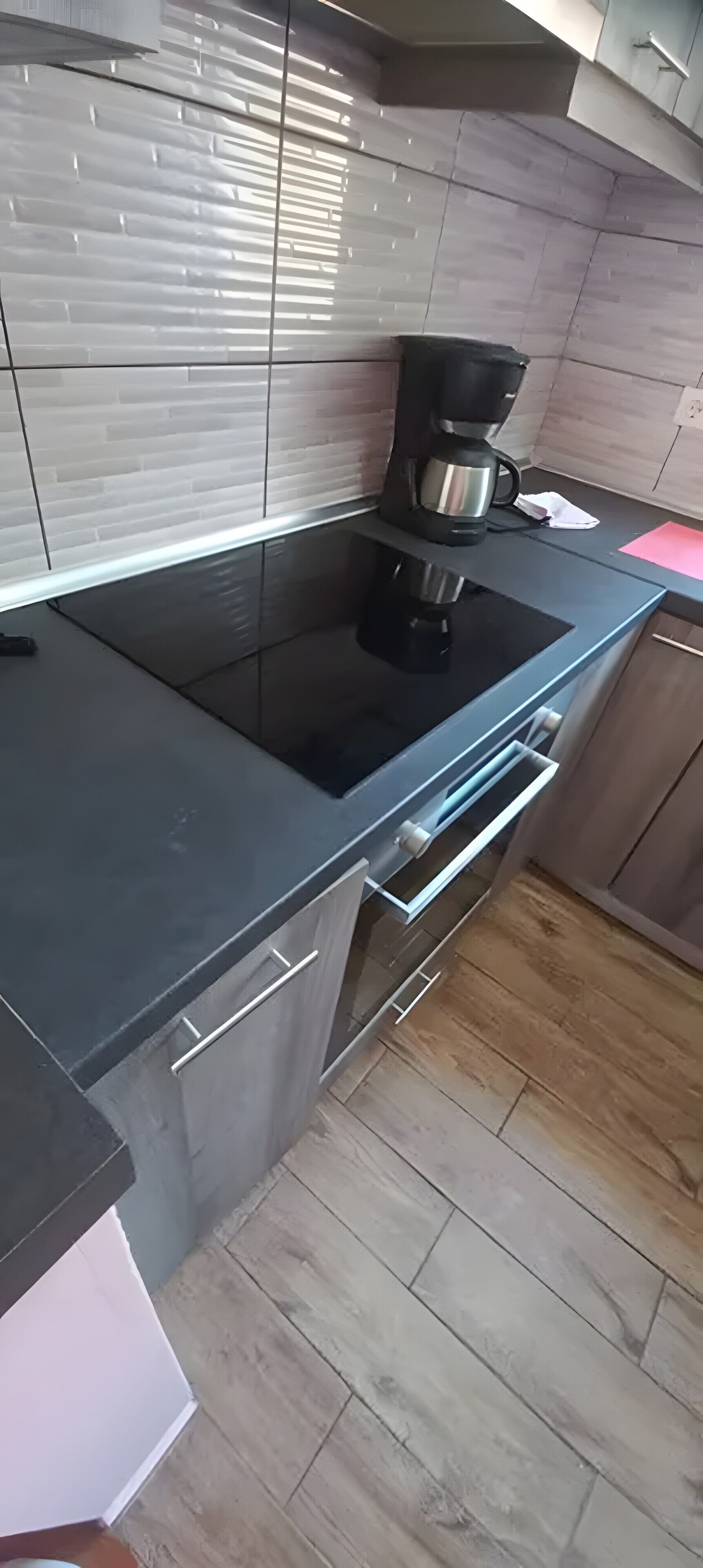Una cocina con encimera negra, cafetera y salpicadero de azulejos.