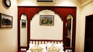 Habitación de hotel con una cama, un reloj, aire acondicionado, cuadros enmarcados y un espejo.