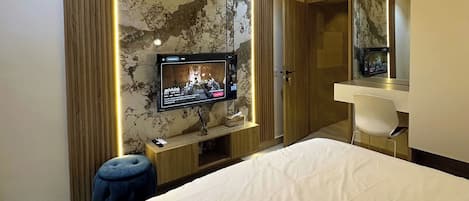 A modern hotel room with a large bed, a TV mounted on a marble wall, a desk with a chair, and a wardrobe.