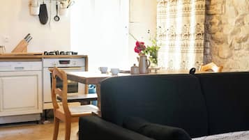 Une cuisine équipée d’une cuisinière, d’un four et d’ustensiles, une table à manger avec des chaises, un canapé et un vase décoratif avec des fleurs.