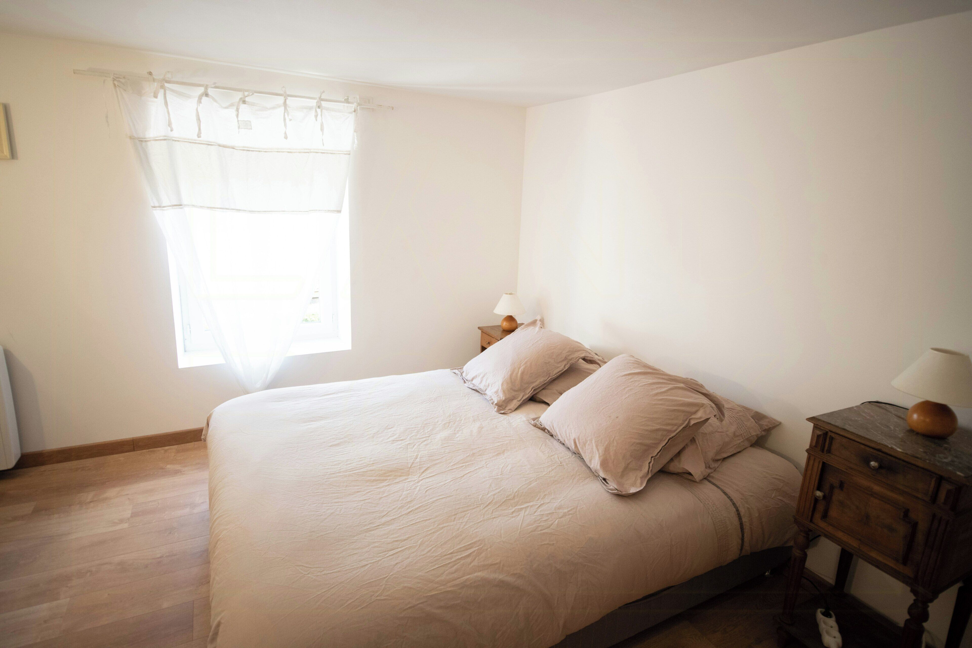 Un dormitorio con una cama, una mesita de noche, una lámpara y una ventana con cortinas.