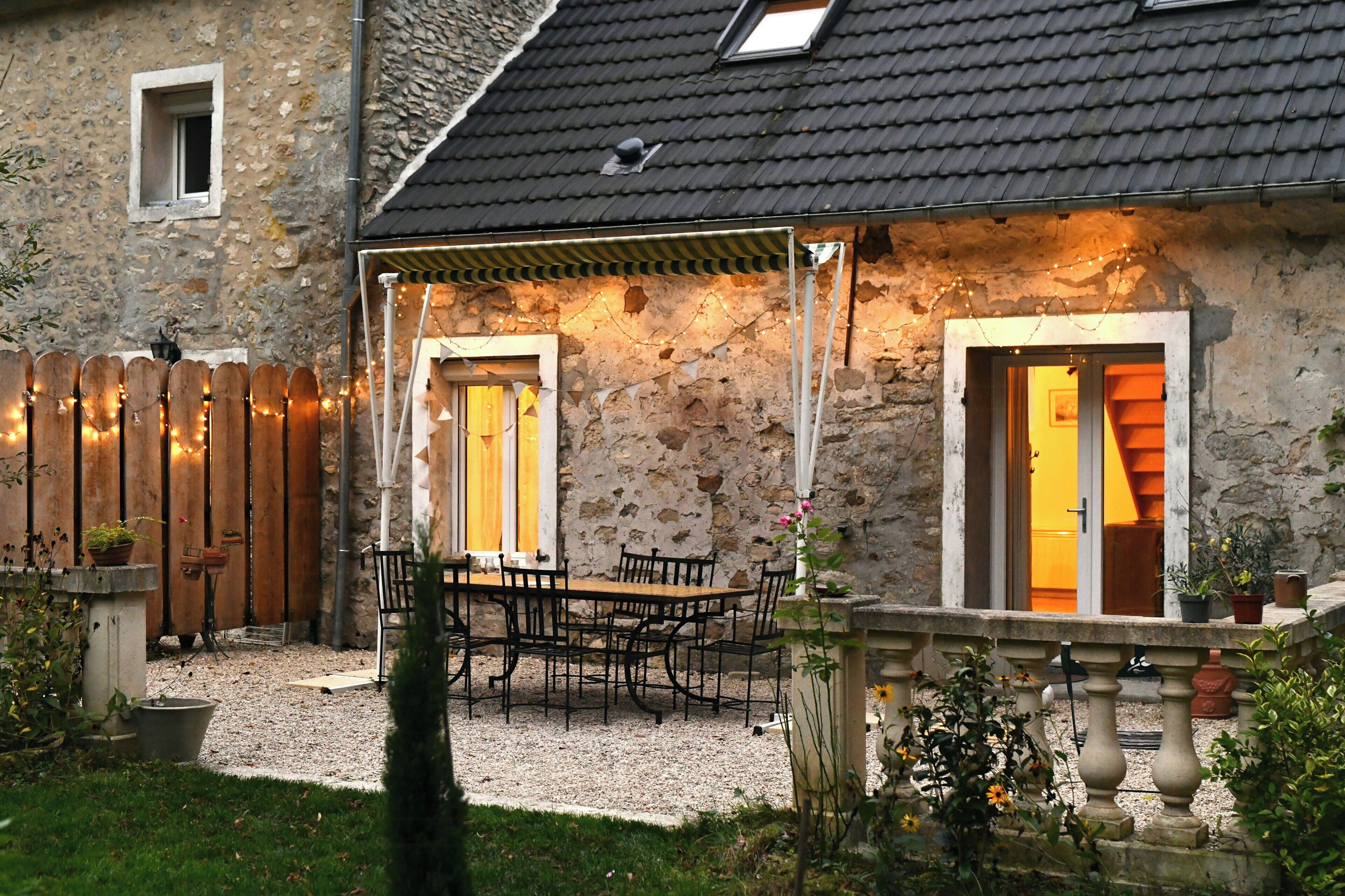 Une maison en pierre dotée d’un patio couvert, d’une clôture en bois et d’un espace extérieur aménagé pour s’asseoir.